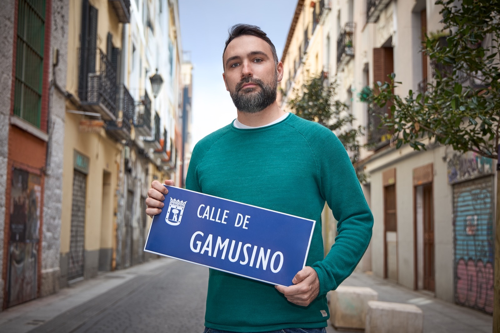 Fernando de Córdoba en una calle de Madrid sujetando una placa que dice «Calle de Gamusino»